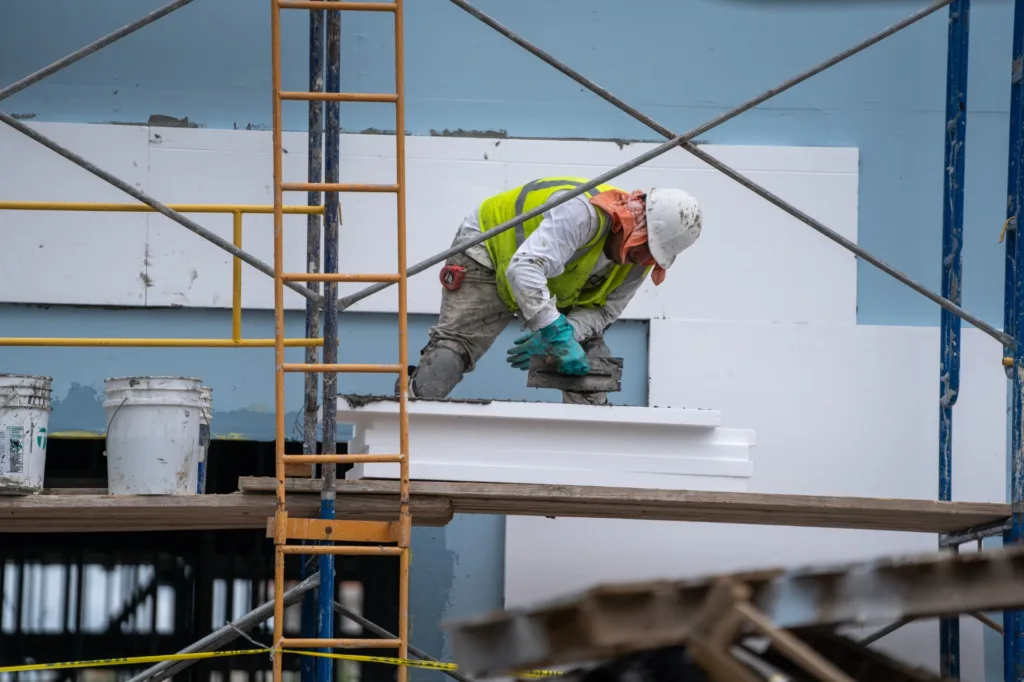 Construction worker installing insulation on scaffolding