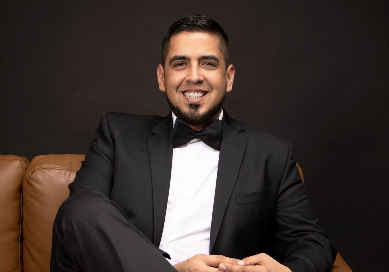 Smiling man in tuxedo seated on leather sofa