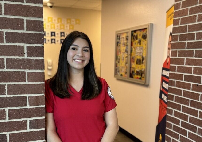 Smiling woman in red scrubs between brick columns