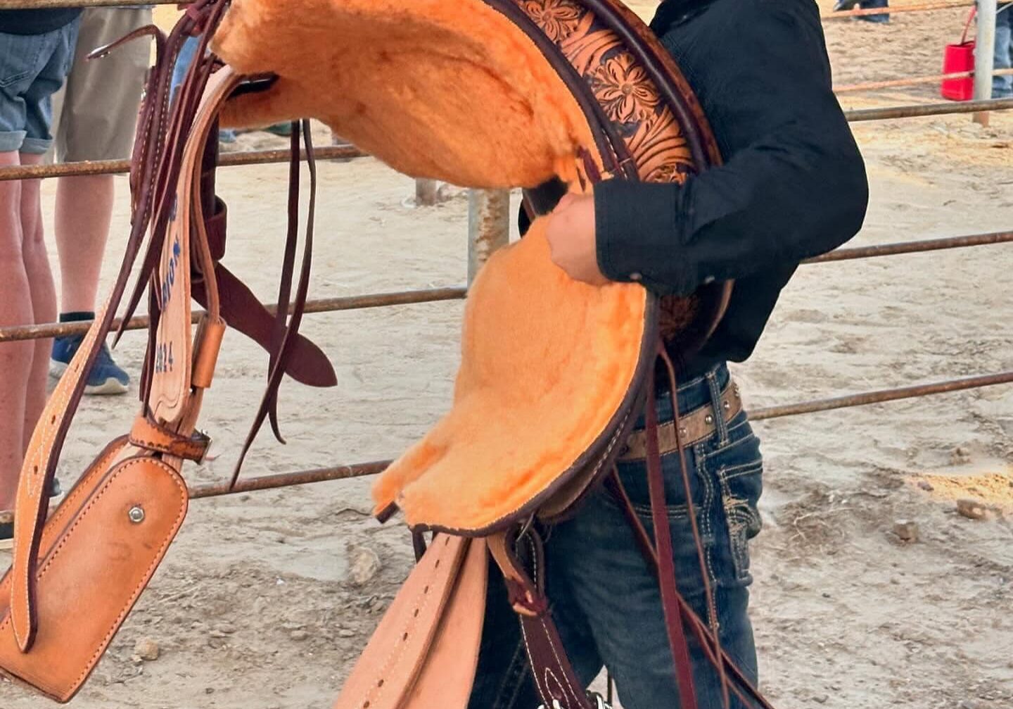 Young boy carrying western saddle at rodeo