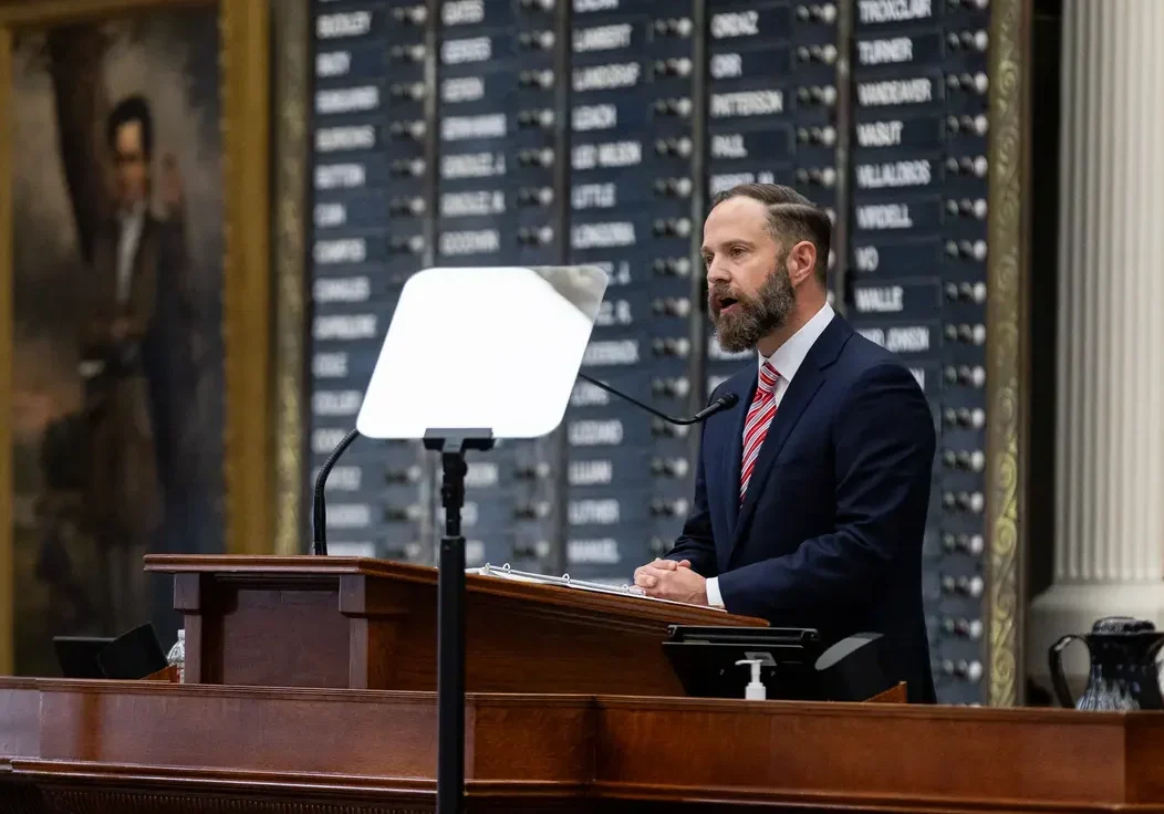 Man speaking at legislative podium with teleprompter