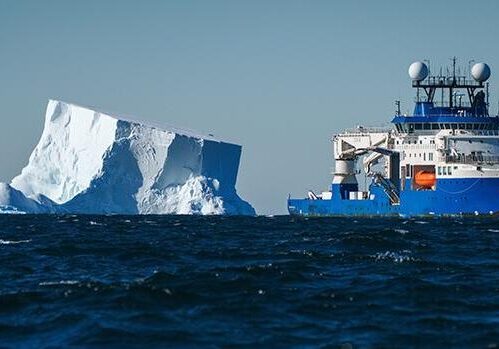 Blue research ship beside large iceberg