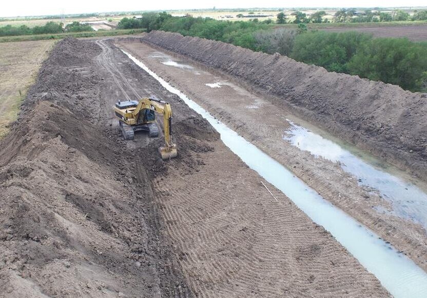 Excavator digging long muddy irrigation canal