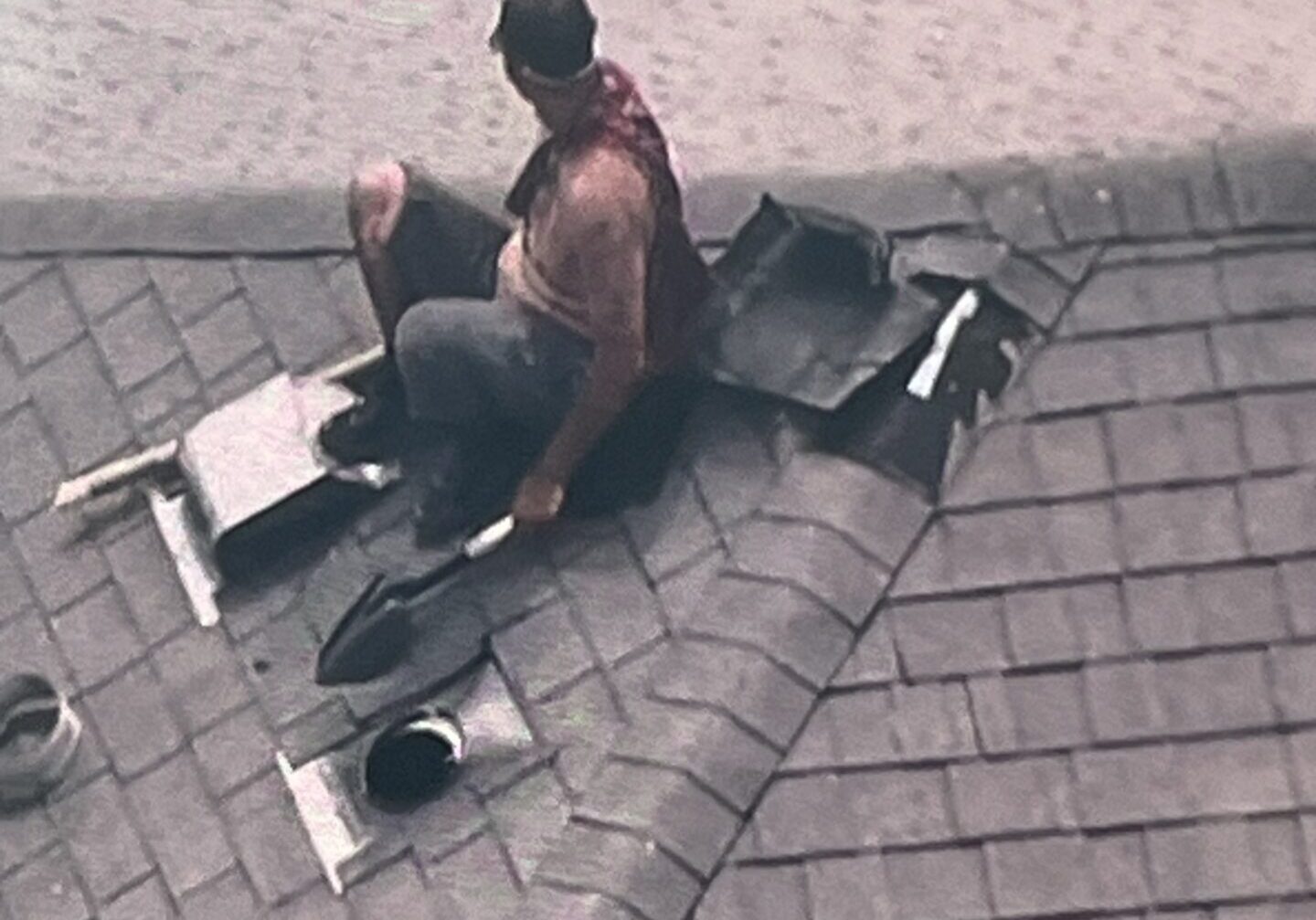 Roofer kneeling on shingled roof repairing vent
