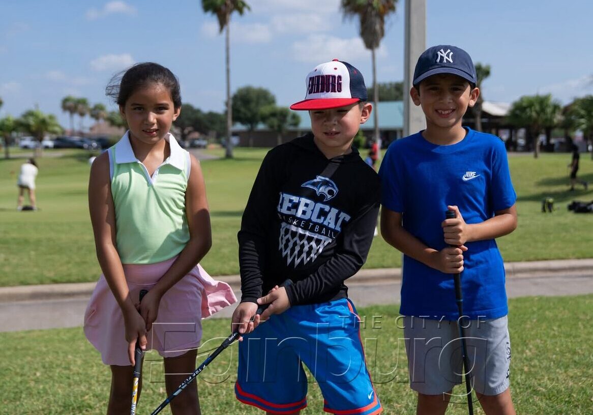 Three children holding golf clubs on course