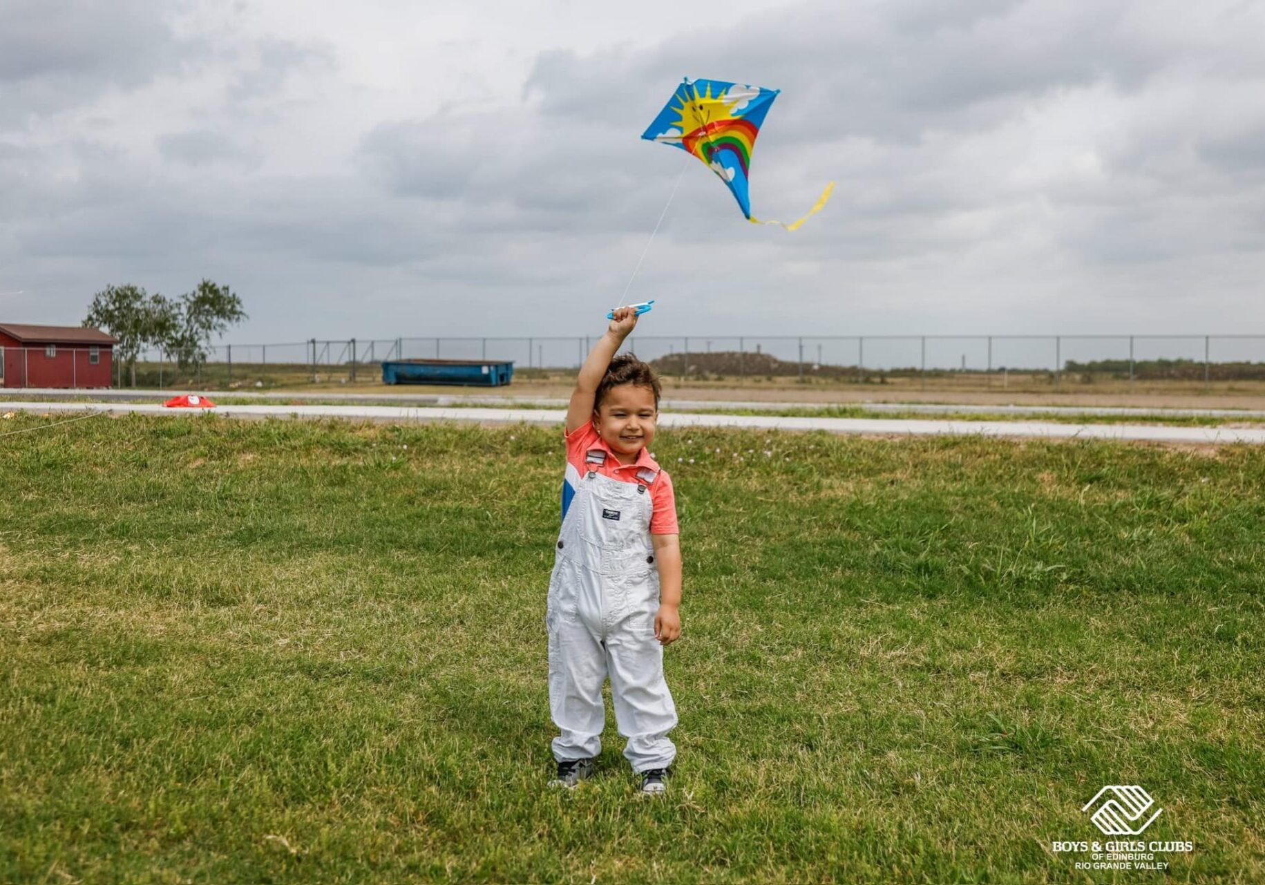 Smiling child flying colorful kite in grassy field