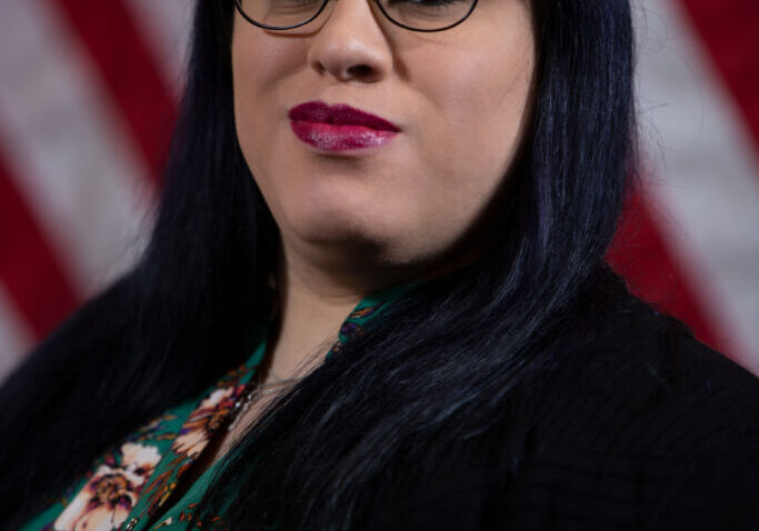 Person with glasses, dark hair, American flag