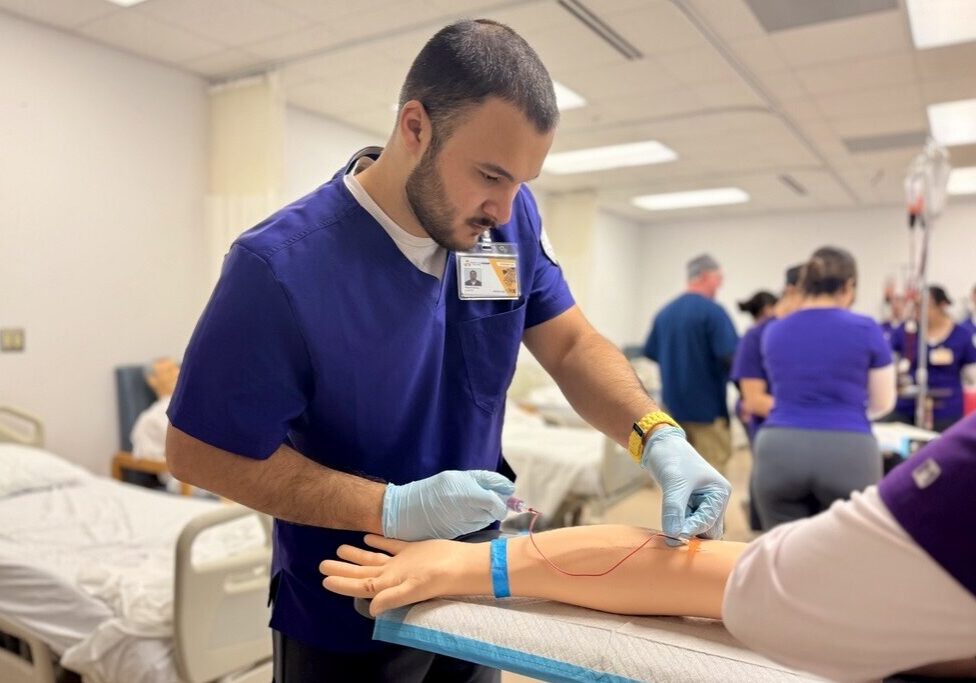 Nursing student inserting IV into training arm