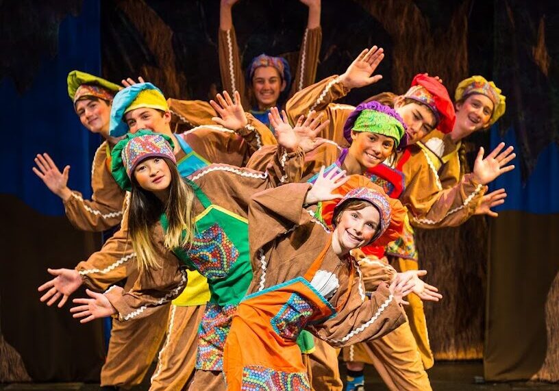 Smiling performers in colorful folk costumes dancing onstage