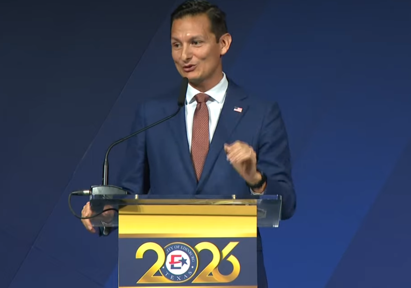 Man speaking at podium with 2026 sign