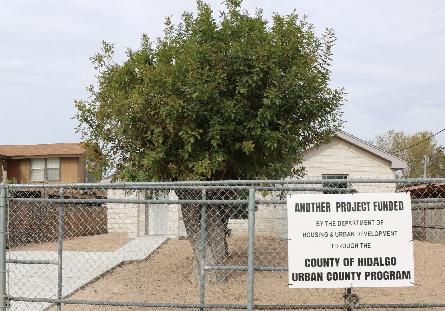 House behind chain-link fence with funding sign