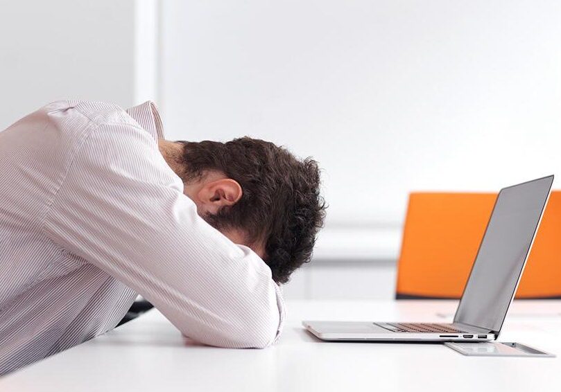 Exhausted man asleep at desk with laptop