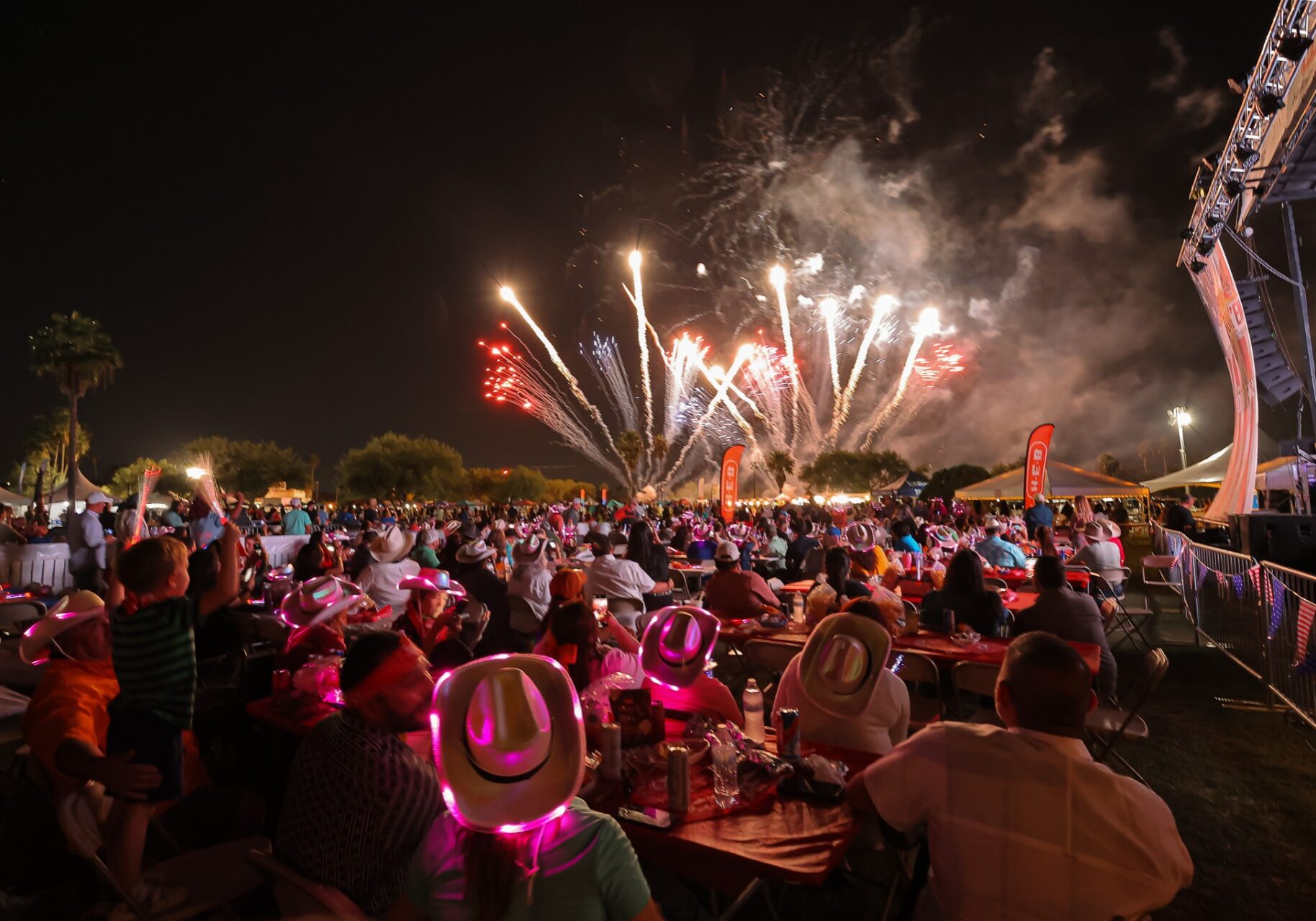 Crowd watching fireworks with glowing pink cowboy hats